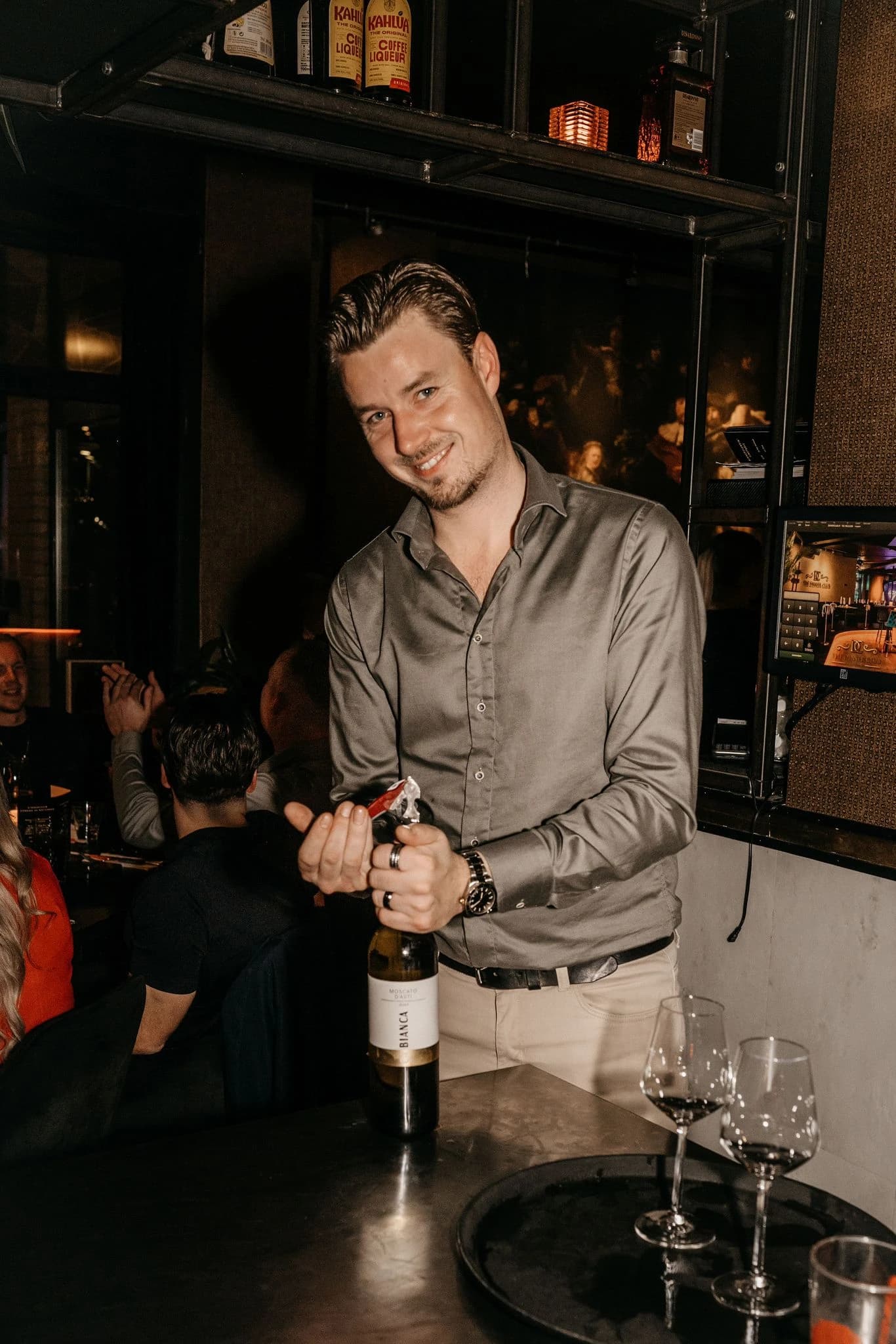 Een medewerker opent een fles wijn aan de bar