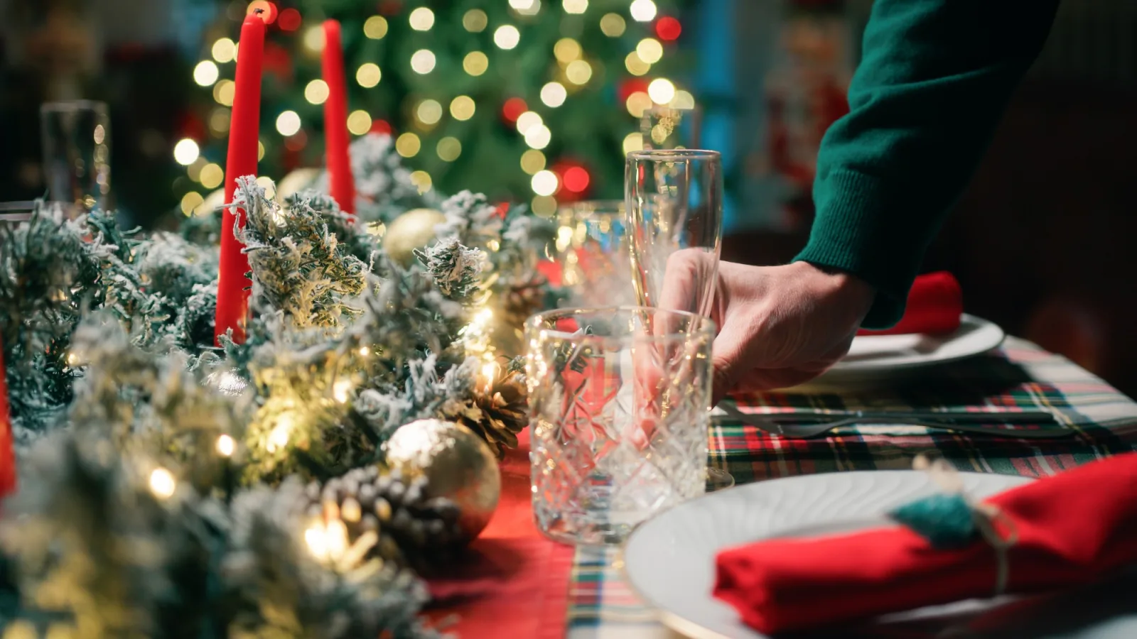 Een feestelijk gedekte kersttafel met rode kaarsen, kristallen glazen en kerstverlichting